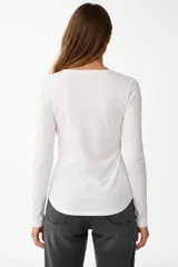 Remera blanca de manga larga, entallada, con cuello redondo y una hilera de botones en el frente. Incluye un pequeño bolsillo decorativo en el pecho.