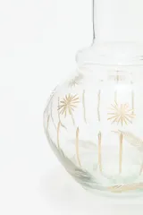 Jarra de vidrio transparente con diseño de estrellas doradas. Incluye un vaso de vidrio transparente con diseño de líneas verticales doradas.