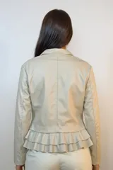 Chaqueta entallada de eco cuero color beige, con cierre frontal asimétrico y detalle de volados en la parte inferior trasera.