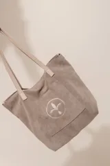 Bolso tipo tote bag de gamuza azul con asas de cuero marrón y bolsillo externo con logo bordado.