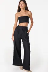 Pantalón de lino blanco de corte ancho y fluido, con cintura alta que incorpora una sobrepretina ancha desmontable con pliegues horizontales.