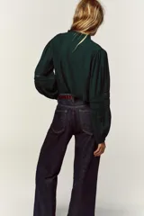 Camisa verde oscuro con cuello de volante y manga larga, detalles de entredoses a tono y cierre frontal con botones forrados.