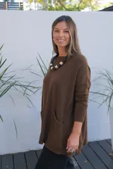 Sweater de tejido de punto en color chocolate, con corte holgado, cuello redondo y mangas largas. Presenta un diseño con bolsillos frontales integrados y terminaciones acanaladas en puños y ruedo.