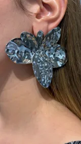 Aros de gran tamaño con diseño de flor de cinco pétalos, realizados en metal plateado con acabado martillado y textura irregular.