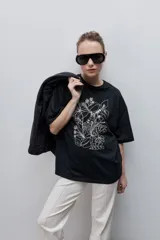 Remera negra de silueta amplia y calce relajado, con cuello redondo, mangas cortas con hombros caídos y estampa botánica en líneas blancas en el frente.