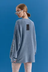 Sweater de punto en color azul grisáceo con diseño oversize. Presenta cuello redondo, mangas largas y detalles de estampados gráficos en el frente y en una de las mangas. El tejido posee un acabado desgastado que le otorga un aspecto vintage.