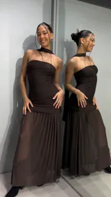 Vestido largo color marrón de silueta ajustada con diseño strapless y tiras cruzadas al cuello, confeccionado en tejido texturizado con falda larga semitransparente.