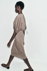 Vestido midi de tejido piqué en color marrón oscuro jaspeado, con escote en pico cruzado y mangas cortas. Presenta detalle de frunces en la cintura y un cinturón integrado con hebilla metálica a contraste.