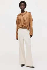Sweater de punto fino color marrón, de cuello redondo con ribetes en canalé. Presenta un diseño que incluye un fular a juego anudado alrededor de los hombros, simulando el efecto de otro jersey sobrepuesto.