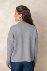 Buzo de punto color visón con cuello alto, manga larga y diseño holgado. Presenta un bordado floral en relieve al tono en la parte frontal.