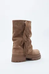 Bota de caña media con flecos laterales, confeccionada en material con textura tipo gamuza. Presenta una silueta relajada y suela robusta con base dentada.