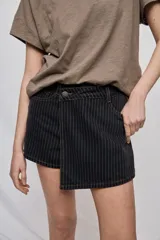 Falda short de denim con diseño a rayas verticales y costuras en contraste. Presenta frente asimétrico con efecto de falda, tiro medio, bolsillos delanteros y cierre con botón.