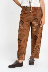 Jean de corte baggy y tiro medio, confeccionado en algodón peinado. Presenta un diseño estampado con motivos florales en tonos tierra sobre una base color marrón.