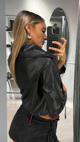 Campera corta de ecocuero negro con textura de efecto cocodrilo, diseño con flecos frontales, solapas anchas y mangas largas.