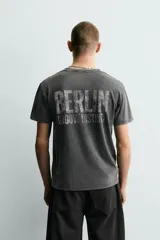 Camiseta de corte slim fit, cuello redondo y manga corta, color gris oscuro con efecto lavado. Presenta un gran estampado frontal con el número "74" en blanco desgastado y pequeños estampados circulares en los hombros.