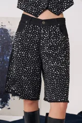 Bermuda de jean negro con tiro medio, largo a la rodilla y ruedo desflecado. Presenta un diseño cubierto de apliques metálicos plateados tipo tachas, con bolsillos funcionales.