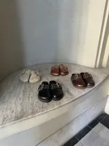 Zueco de cuero color beige, con hebilla metálica y remaches.