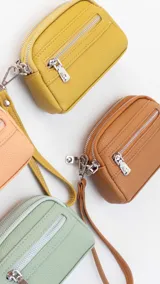 Monedero de dama con correa de mano, confeccionado en material símil cuero con textura granulada. Cuenta con doble compartimento principal con cierre y un bolsillo frontal con cierre, ideal para organizar tarjetas, billetes y monedas.