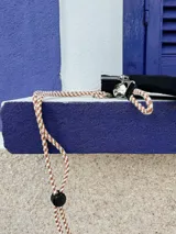 Bandolera negra de nylon con cierre superior y correa larga de cordón trenzado en tonos beige y blanco.