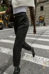 Pantalón de tiro alto y corte tobillero, confeccionado en tejido de aspecto denim oscuro. Presenta diseño de pinzas frontales, bolsillos laterales y cierre frontal con cremallera, botón y gancho. Incluye un cinturón fino a tono con hebilla metálica dorada.