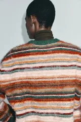 Jersey de punto con diseño de rayas horizontales multicolor en tonos rosados, naranjas, rojos y verdes. Presenta cuello redondo, manga larga y acabados acanalados en color verde oscuro en el cuello, puños y ruedo.