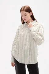Camisa de algodón con diseño de rayas verticales finas en tonos neutros, corte holgado, cuello camisero y cierre frontal con botones.