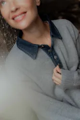 Buzo de punto gris con cuello camisero de denim y cierre frontal parcial con botones metálicos. Presenta mangas largas y un diseño de calce holgado.