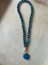 Collar con dije de corazón facetado en color verde esmeralda, con cadena de cuentas de cristal facetadas en tonos amarillos y dorados.