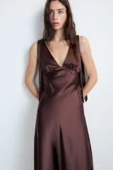 Vestido midi satinado color marrón, con escote en V y tirantes anchos ajustables con lazada en los hombros. Presenta cierre lateral con cremallera oculta.