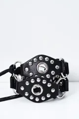 Cinto negro de cuero sintético con diseño de tiras anchas, argollas metálicas y tachas plateadas.