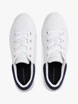 Zapatillas de tenis minimalistas Tommy Hilfiger, confeccionadas en piel napa blanca con suela gruesa tipo cupsole. Presentan un diseño de corte bajo con cordones, detalle de panel azul marino en el talón y logo metálico de la marca en el lateral.