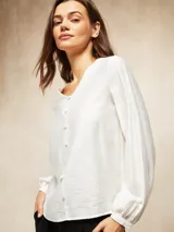 Blusa de color blanco hueso con escote en V y cierre frontal de botones pequeños. Presenta mangas largas con puños ajustados y un diseño de corte recto.