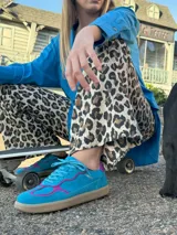 Championes Cherie de estilo deportivo vintage, confeccionados en cuero vacuno y gamuza. Presentan una combinación de colores en azul vibrante con detalles en fucsia intenso, suela sintética plana y flexible, y logo de la marca grabado en dorado en el lateral.