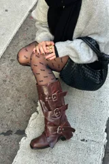Botas de caña media en cuero color chocolate con acabado gastado. Presentan tres correas horizontales con hebillas metálicas ajustables y un diseño de solapas superpuestas. Cuentan con taco cuadrado bajo.