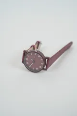 Reloj analógico con correa de cuero sintético color rosado pálido y caja a juego. La esfera es beige claro con números romanos en negro.
