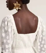Vestido largo evasé de crepé blanco con textura y volados. Tiene escote corazón, elástico en la cintura, lazo con cordón y borla en las puntas, y mangas cortas.