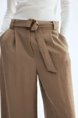 Pantalón de tiro alto con corte holgado y piernas amplias, color marrón, con pliegues delanteros y cinturón del mismo tejido con hebilla circular.