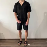 Camisa de tejido de punto calado color negro, con cuello solapa, cierre frontal de botones y mangas cortas.
