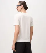 Remera blanca de manga corta y cuello redondo, confeccionada en algodón con bordados florales en tono oscuro aplicados en los hombros.