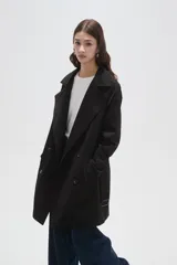 Trinchera de corte clásico, color negro, con cierre frontal de doble botonadura, solapas amplias y cinturón ajustable con hebilla en la cintura.