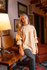 Blusa color beige de corte holgado, cuello alto con volados y mangas largas abullonadas con elástico en los puños.