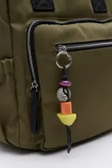 Mochila de nylon negra con asas superiores reforzadas y tiras regulables. Cuenta con un bolsillo frontal con cierre metálico y un detalle colgante de cuentas de colores. Los laterales tienen bolsillos elastizados y el compartimento principal tiene cierre.