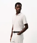 Remera polo masculina de manga corta en color blanco, confeccionada en punto texturizado. Presenta cuello polo con cierre frontal de botones y detalles de rayas en el cuello.