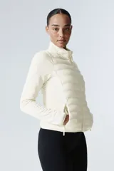 Campera híbrida color crema, con cuerpo acolchado y mangas de tejido elástico. Presenta cuello alto, cierre frontal y bolsillos laterales con cierre.