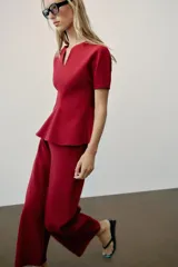 Top peplum confeccionado en hilatura de algodón de color bordó, con escote en V pronunciado, mangas cortas abullonadas y bajo con vuelo.