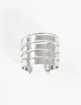 Pulsera ancha tipo brazalete de metal plateado, con diseño de varias vueltas superpuestas y textura martillada. Presenta una abertura frontal con terminaciones en forma de esfera.