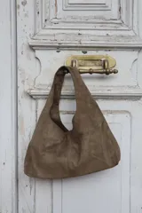 Cartera tipo hobo de gamuza color marrón, con diseño minimalista y asa integrada.