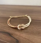 Pulsera ajustable confeccionada a mano con cuentas Miyuki en tonos beige y dorado cobrizo, formando un nudo central.