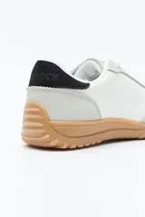 Zapatilla urbana de mujer con silueta retro, combinando paneles de cuero blanco y gamuza gris claro. Posee un talón trasero en gamuza negra y suela robusta de goma color caramelo con relieve.