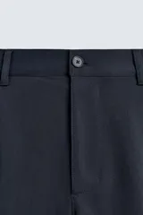 Pantalón de corte recto confeccionado en tejido elástico, con cintura elástica, pliegues frontales, bolsillos laterales y bolsillos traseros de vivo con botón.